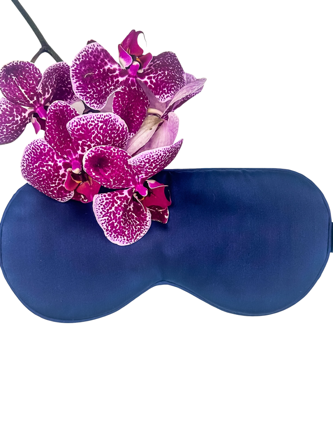 Antifaz para dormir de seda morera color azul marino acompañado de orquídeas moradas