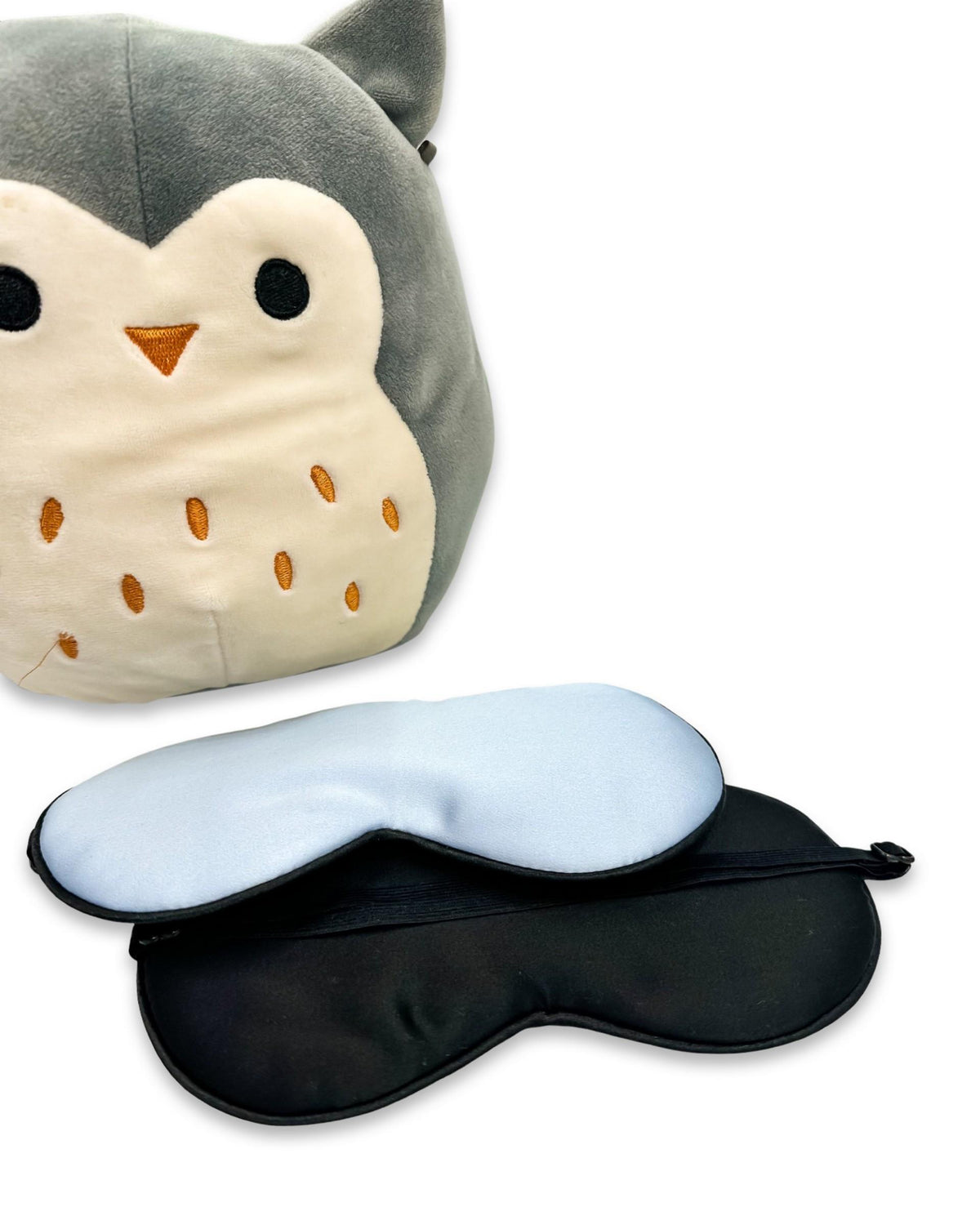 Antifaz de seda infantil azul junto a un peluche de búho, mostrando su parte posterior negra