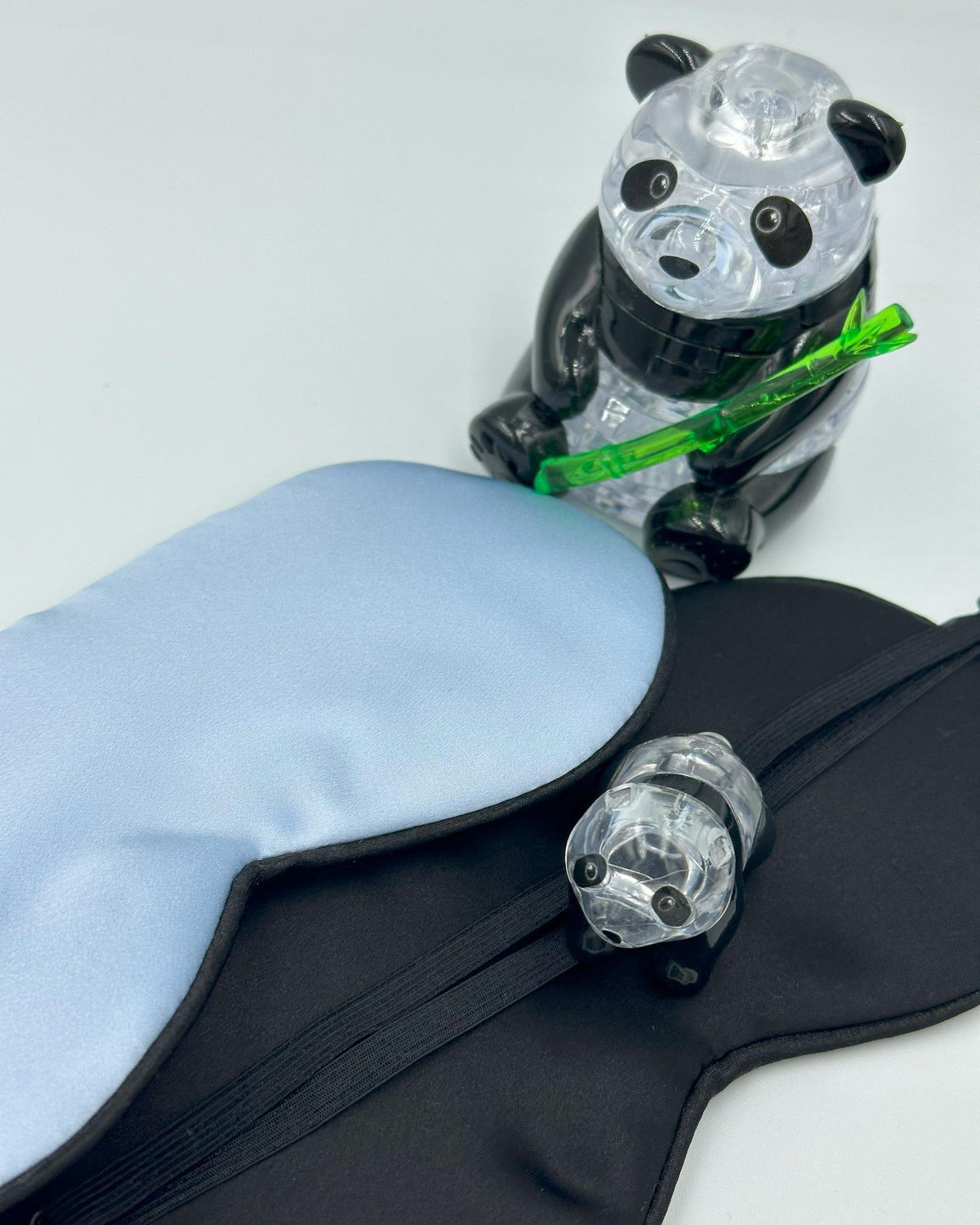 Antifaz de seda infantil azul y su parte posterior negra junto a dos figuras de panda