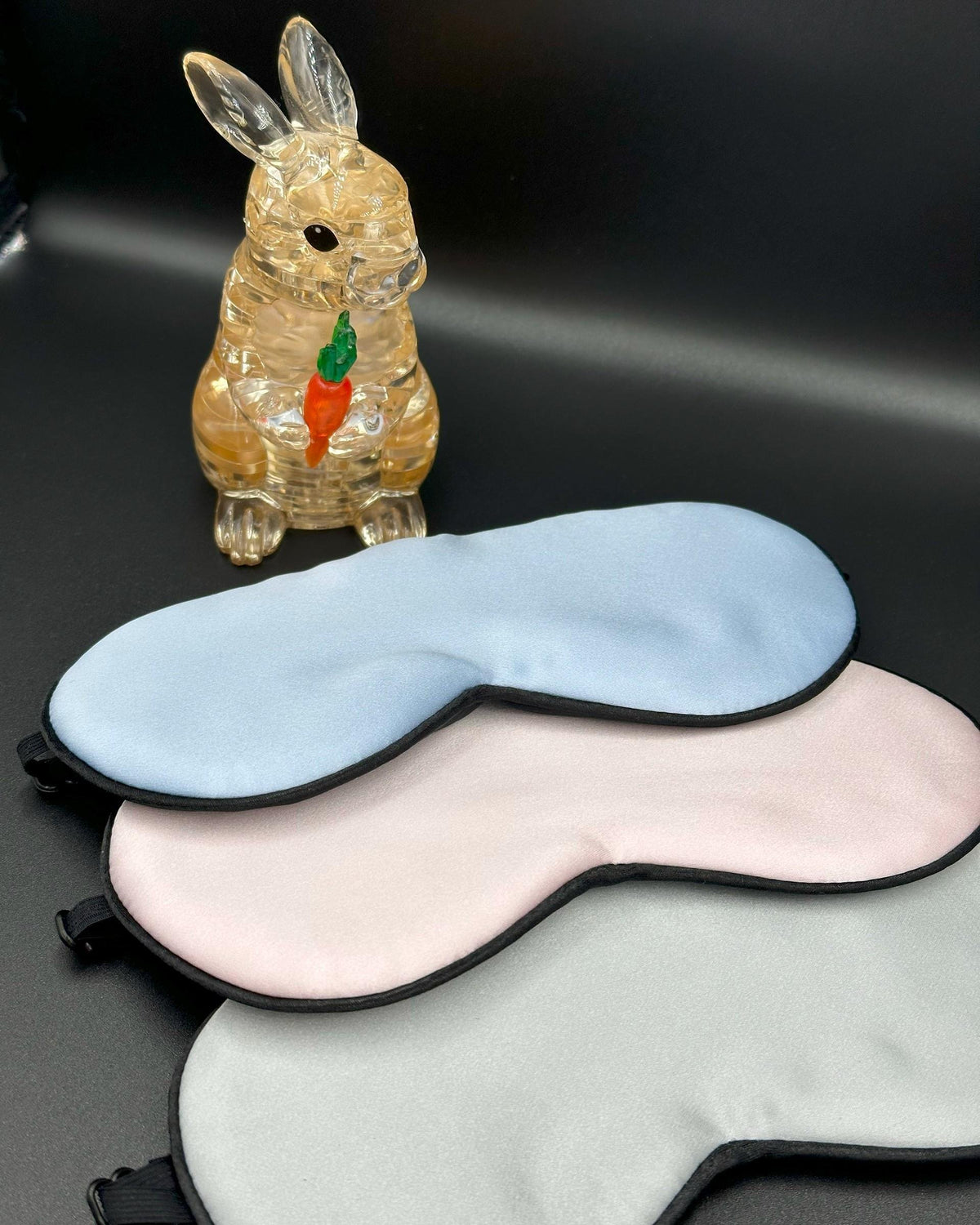 Antifaces de seda para niños en azul, rosa y gris junto a una figura de conejo