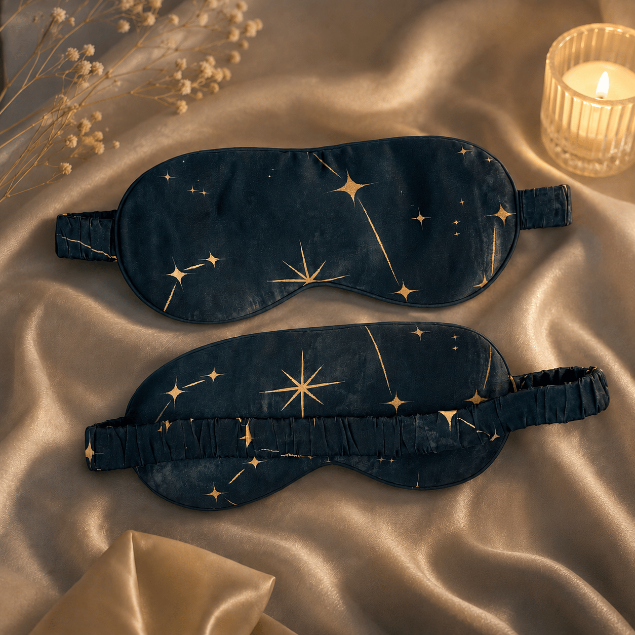 Antifaz para dormir de seda Noche Estrellada con estrellas doradas sobre tejido satinado junto a una vela