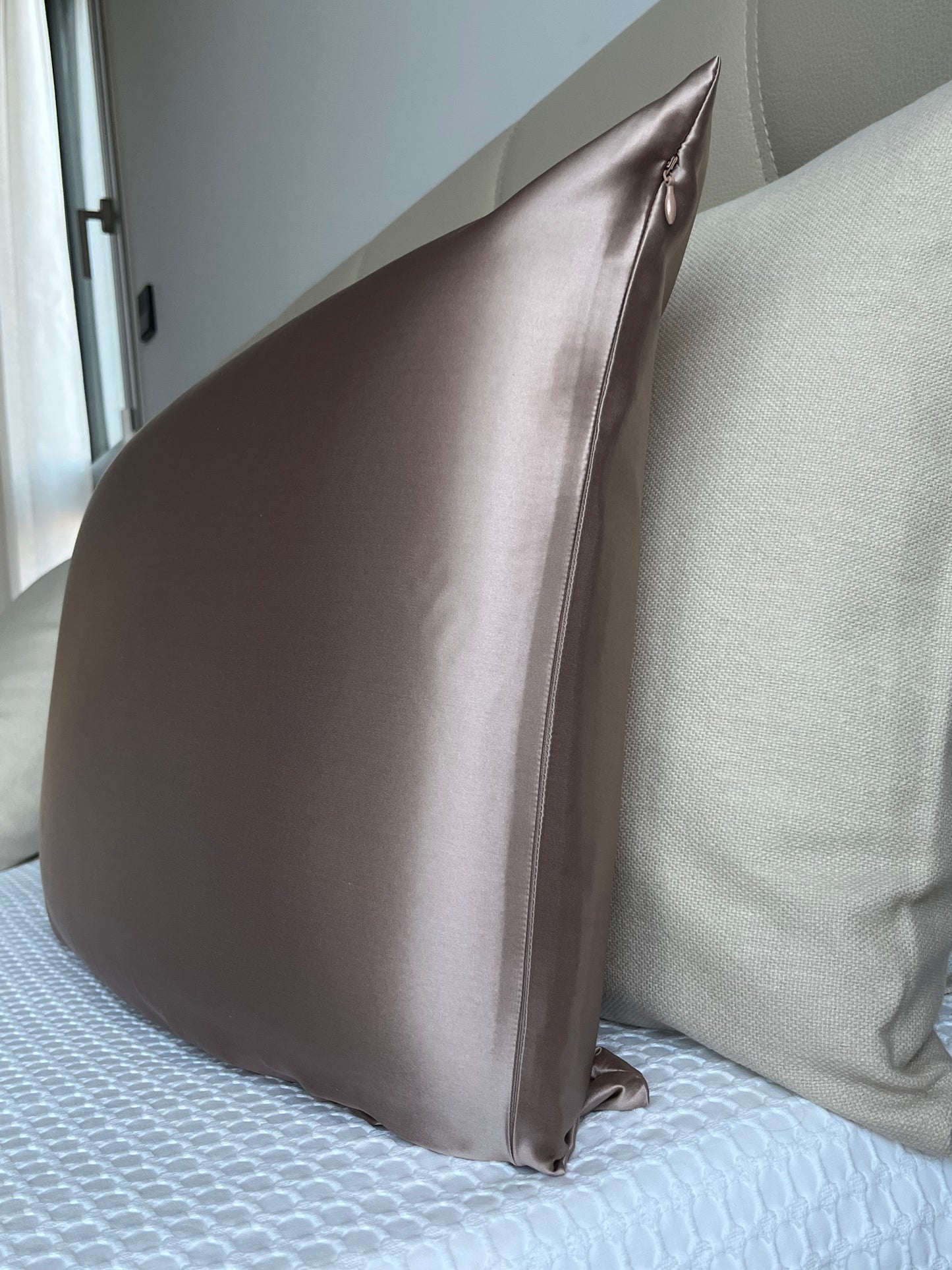 Vista lateral de una funda de almohada de seda de morera color bronce apoyada sobre una cama