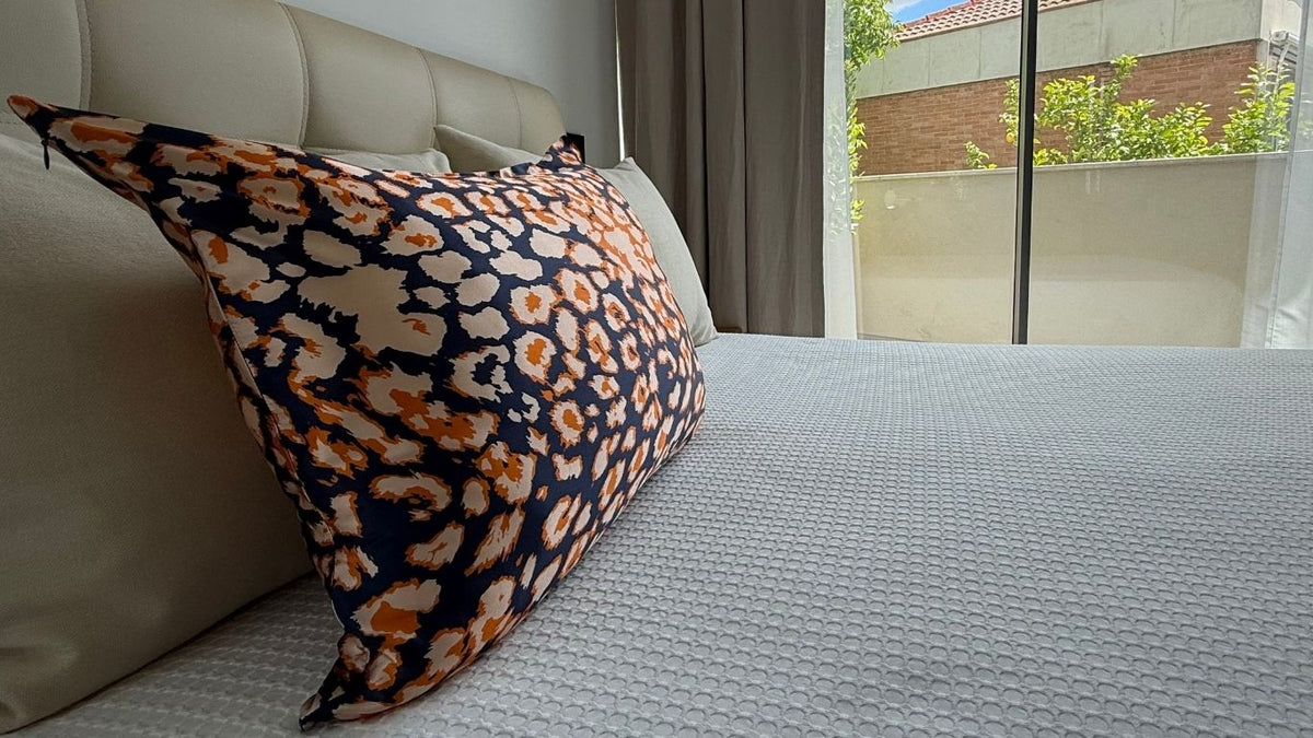 Funda de almohada de seda con estampado animal azul marino, beige y naranja sobre una cama