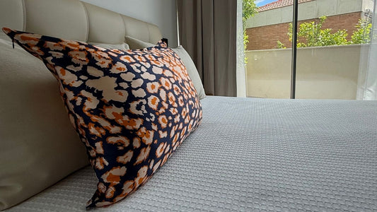 Funda de almohada de seda con estampado animal azul marino, beige y naranja sobre una cama