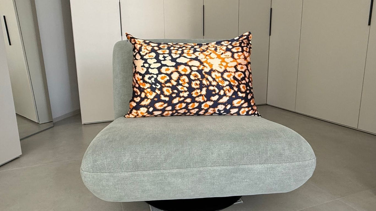 Funda de almohada de seda con estampado animal azul marino, beige y naranja sobre un sillón