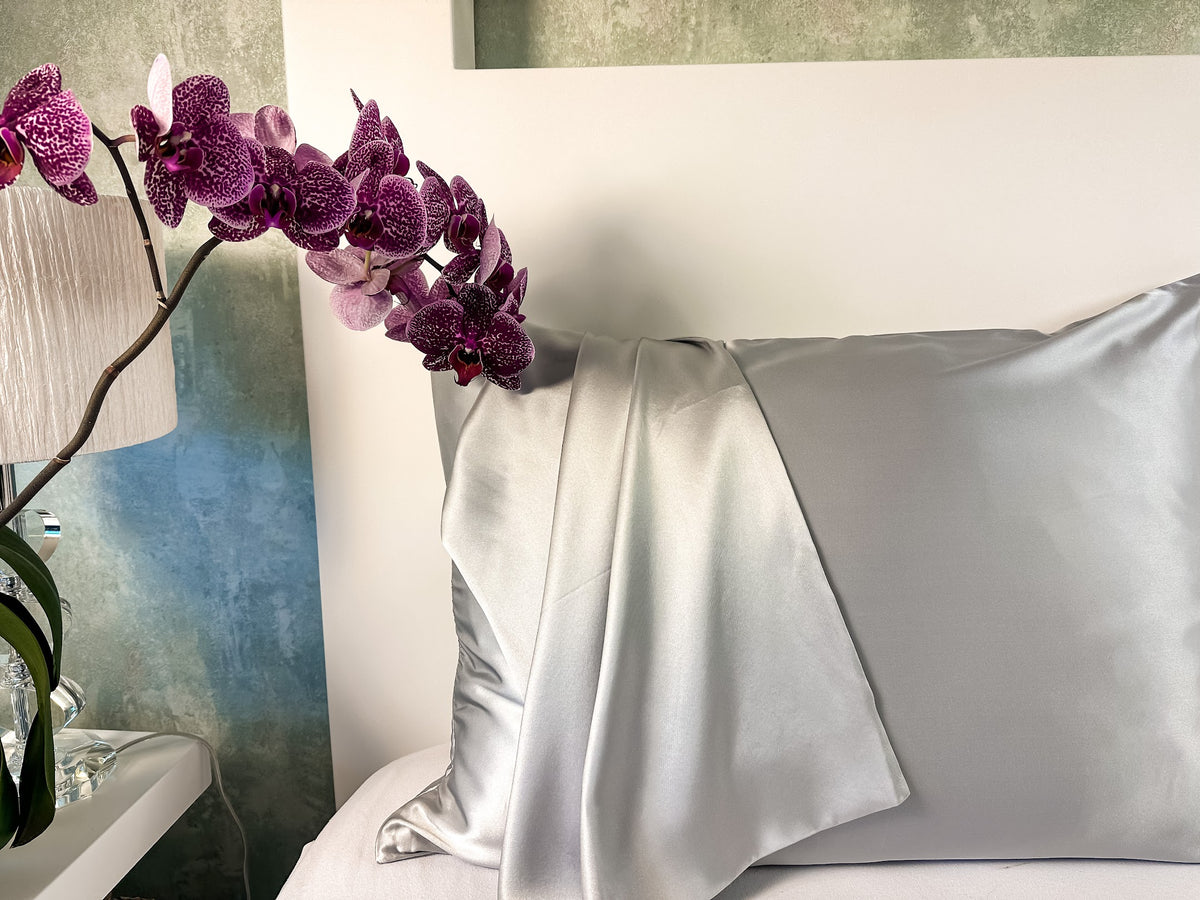 Funda de almohada de seda gris plata junto a una orquídea morada